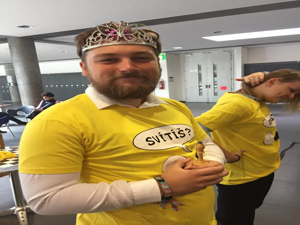 President of ESN MENDELU wearing a yellow Světluška shirt while, a crown and holding the king chess piece