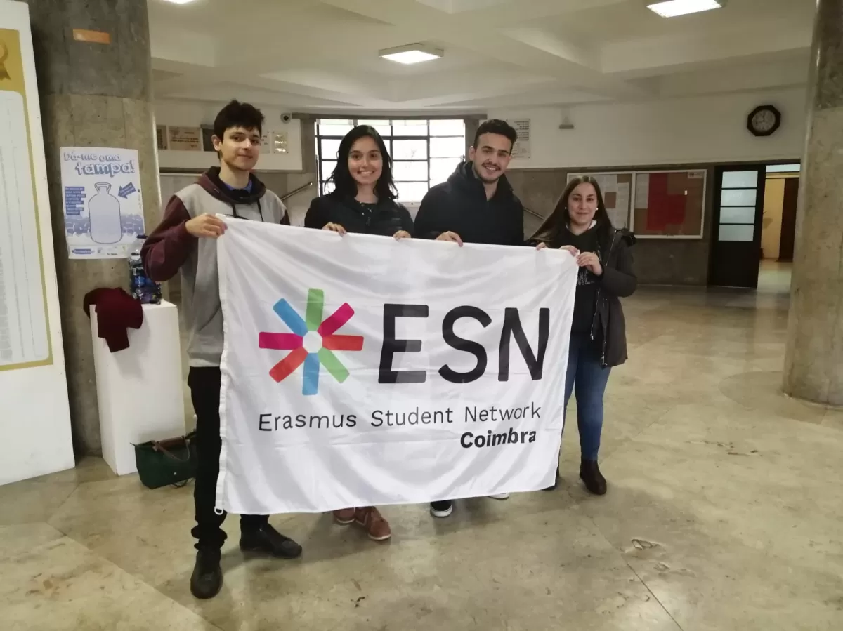ESN volunteers and international students holding the ESN Coimbra flag at the school.