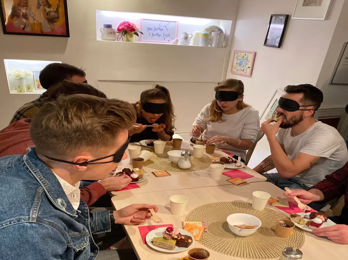 Group of people at the table eating with something on their eyes to simulate being visually impaired.
