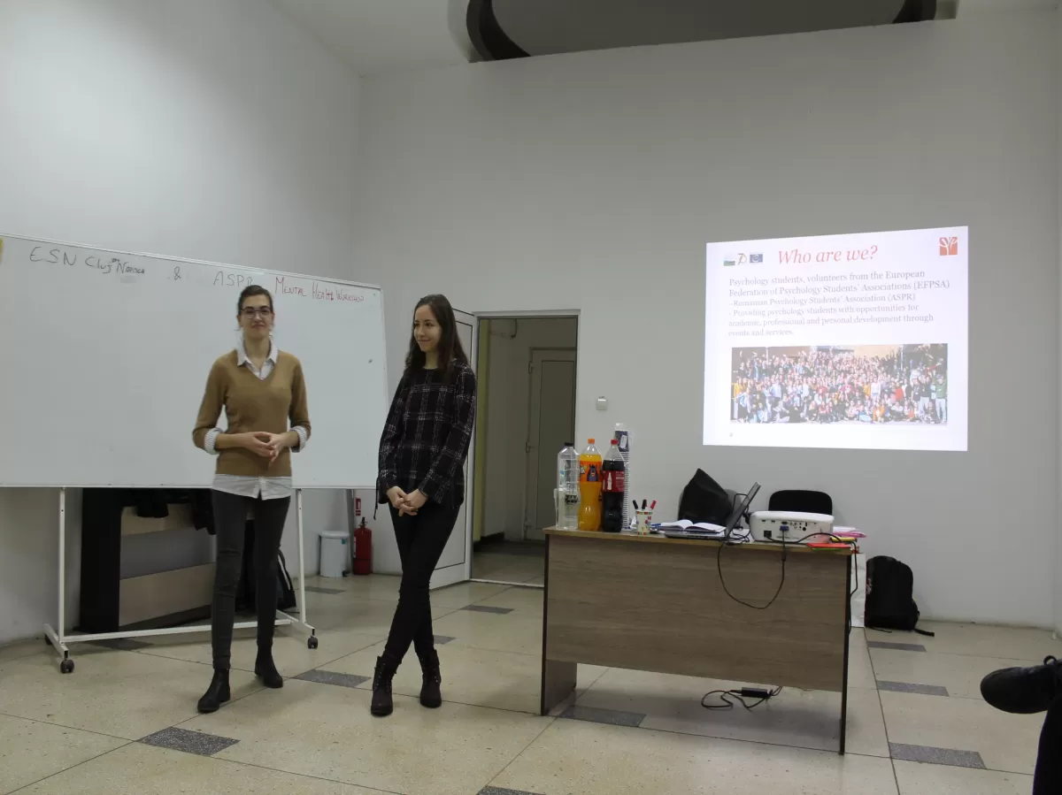 2 trainers standing next to a desk with a power-point presentation in the background.