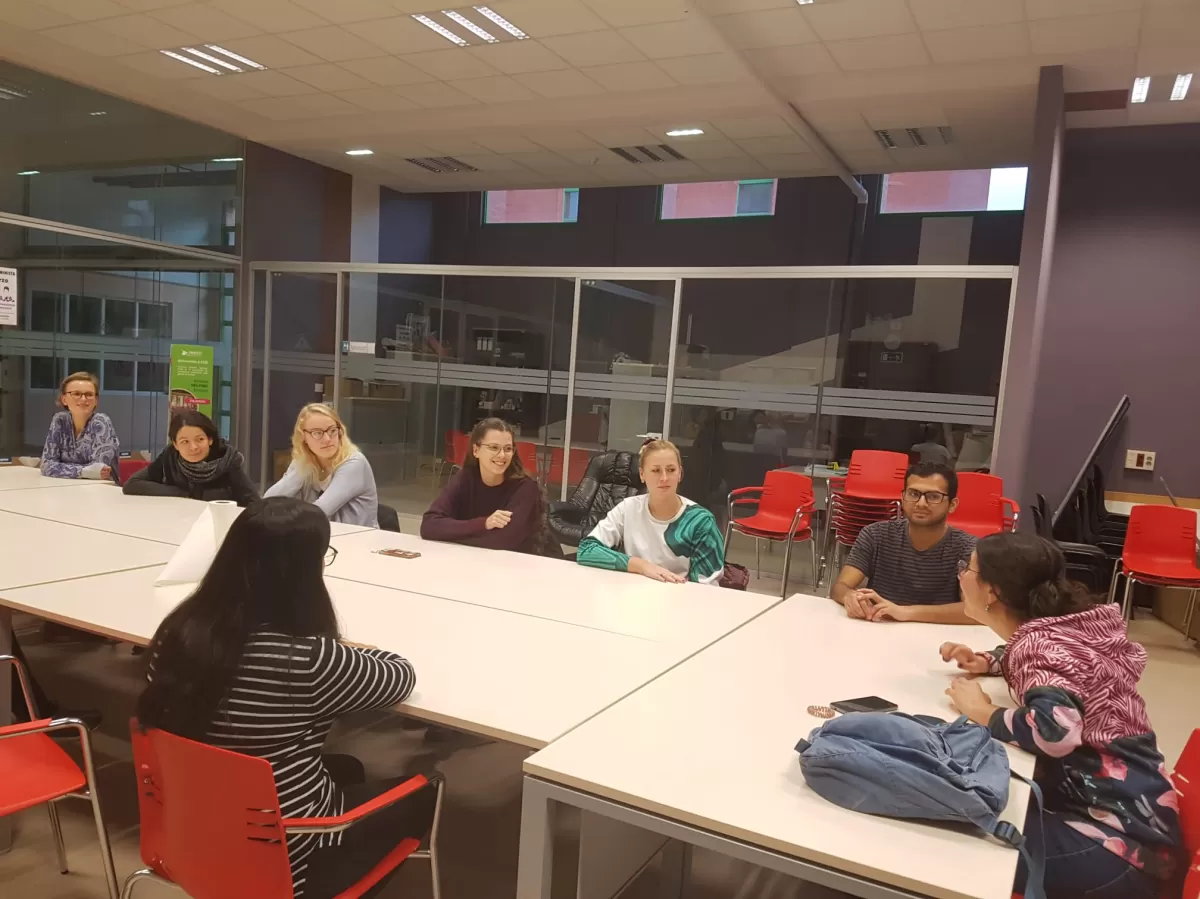 A group of students sitting at a long table listen to a person talking
