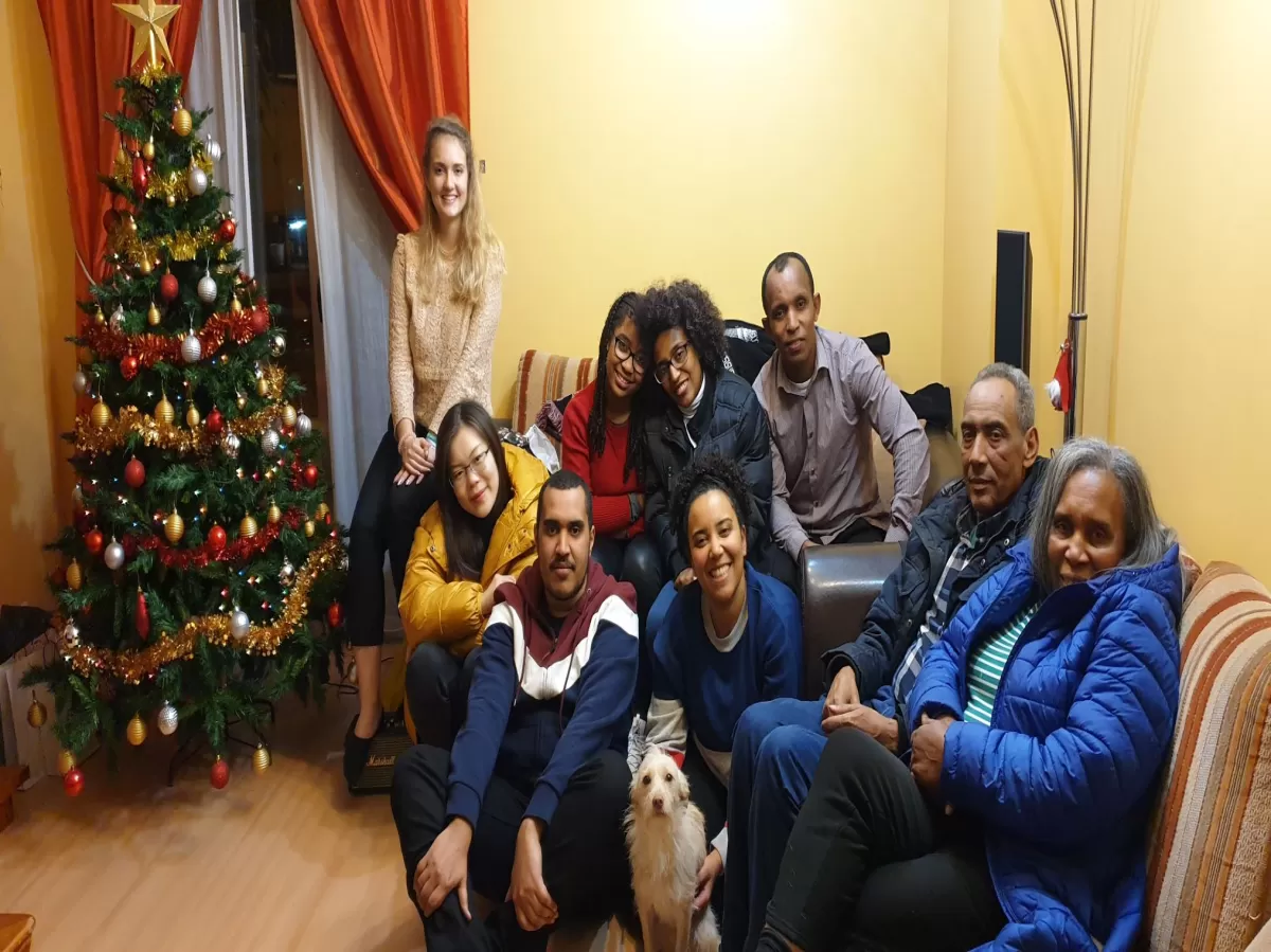 8 people sitting in the sofa by the Christmas tree in a family photo. Two of the people in the photo are international students.