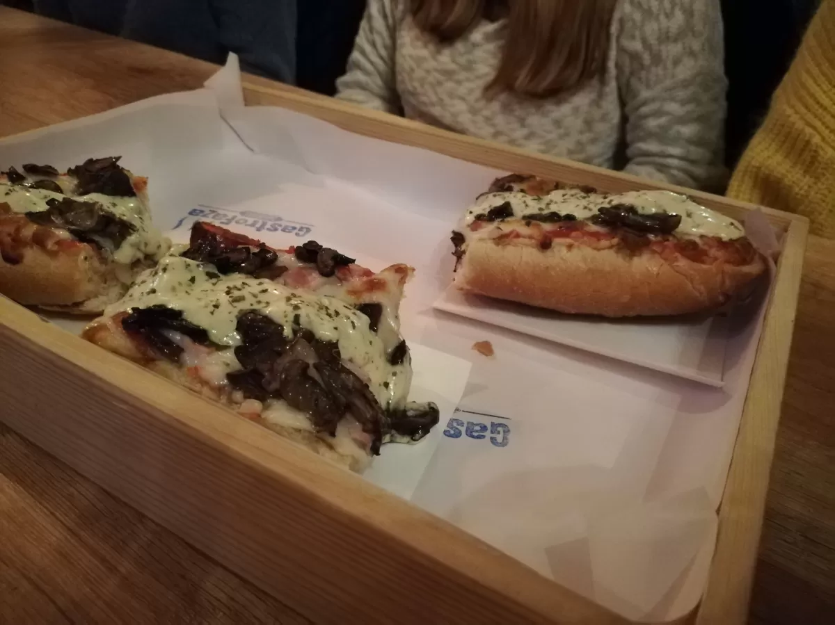 A wooden tray with three pieces of "zapiekanka" - toasted bread with cheese, mushrooms, ham and sauce