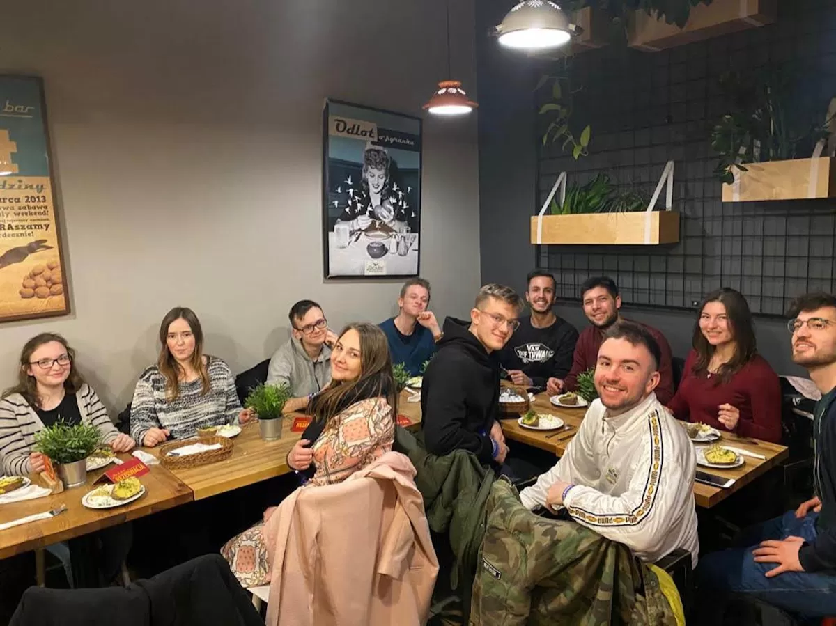 A group of international students sitting at a table in a restaurant with a typical dish "pyra z gzikiem" on their plates.