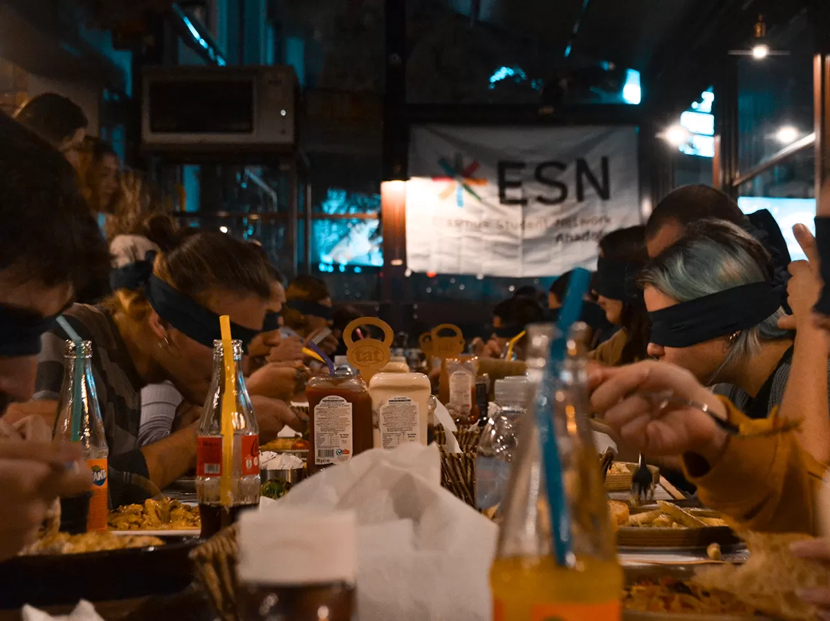 People sitting around a long table and having their dinner with their eyes covered.