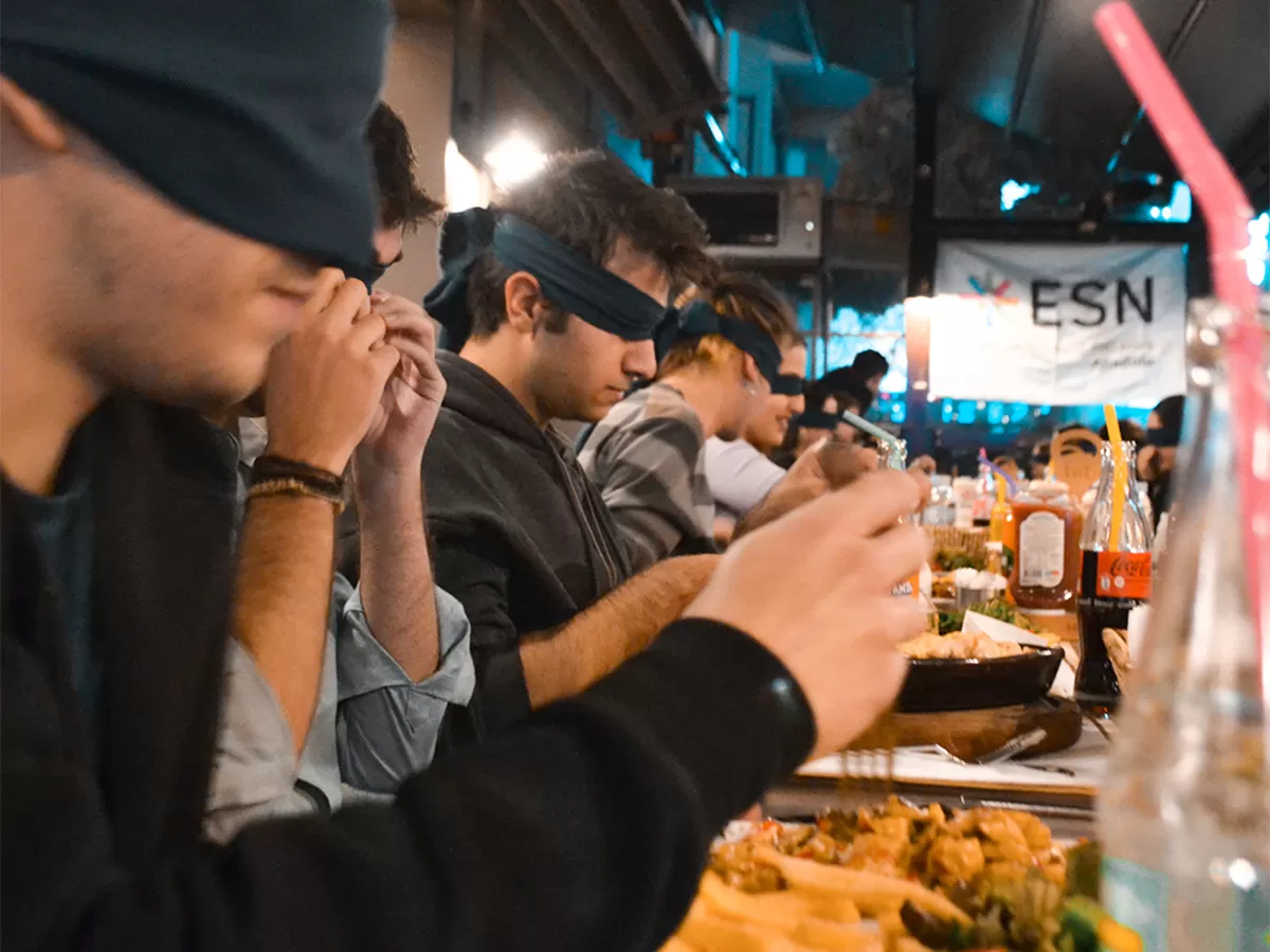 People sitting around a long table and trying to adapt eating without their eyes.