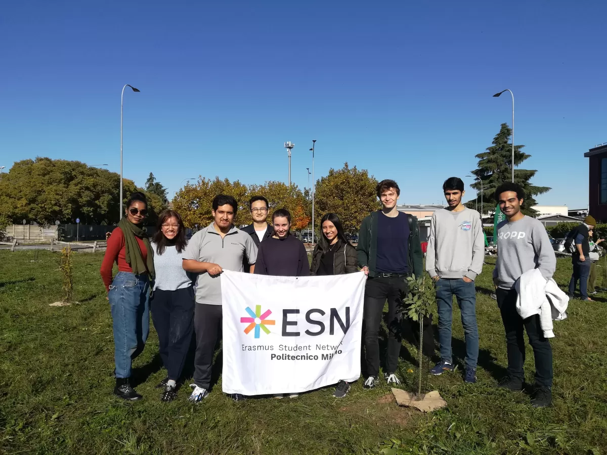 Group of international students and ESNers posing with the ESN flag next to a planted tree