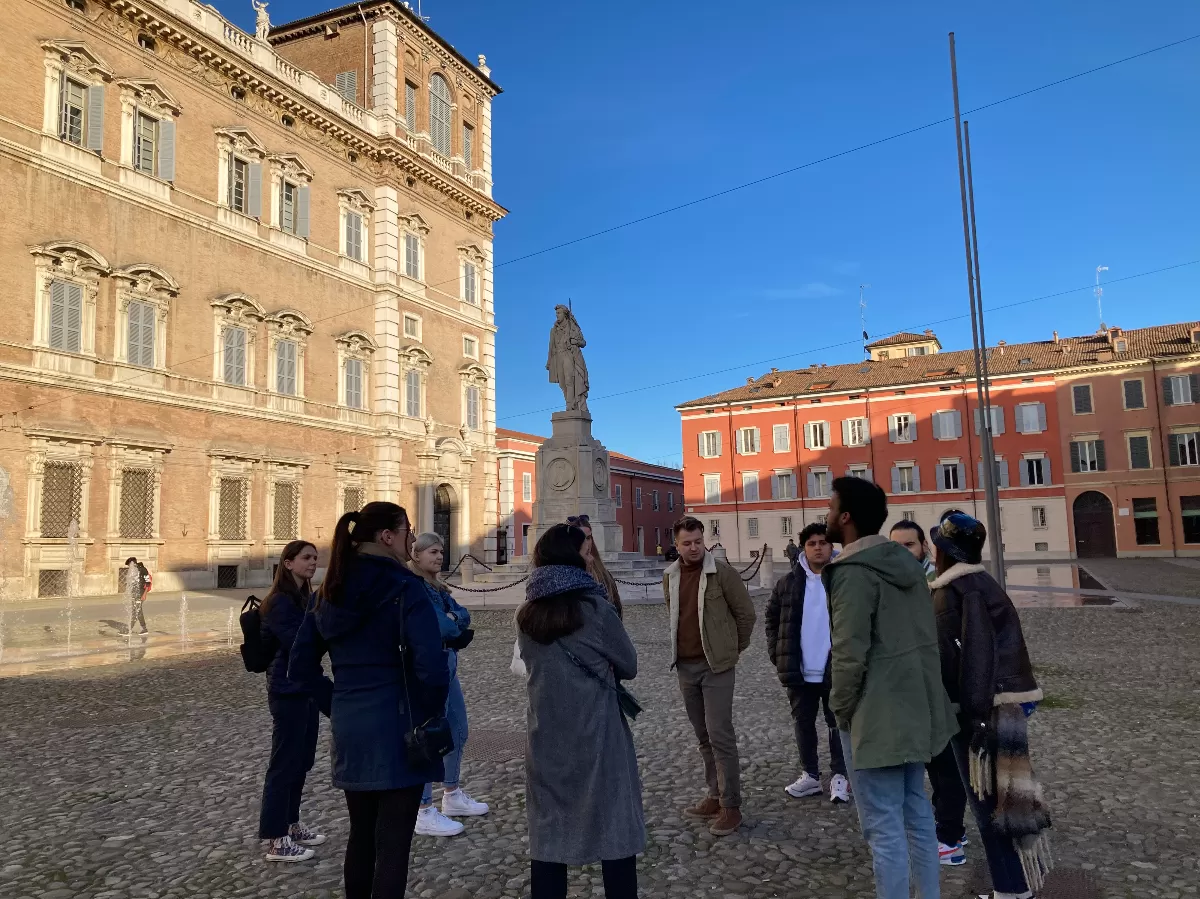 a group of students listening to a guide in Piazza Roma in Modena