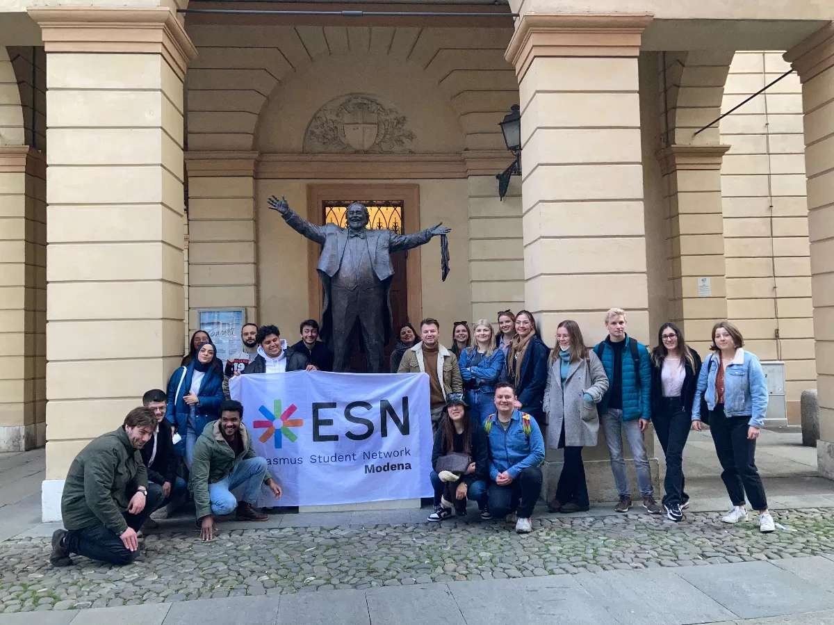 group of international students posing with the flag of ESN Modena in front of the statue of Luciano Pavarotti