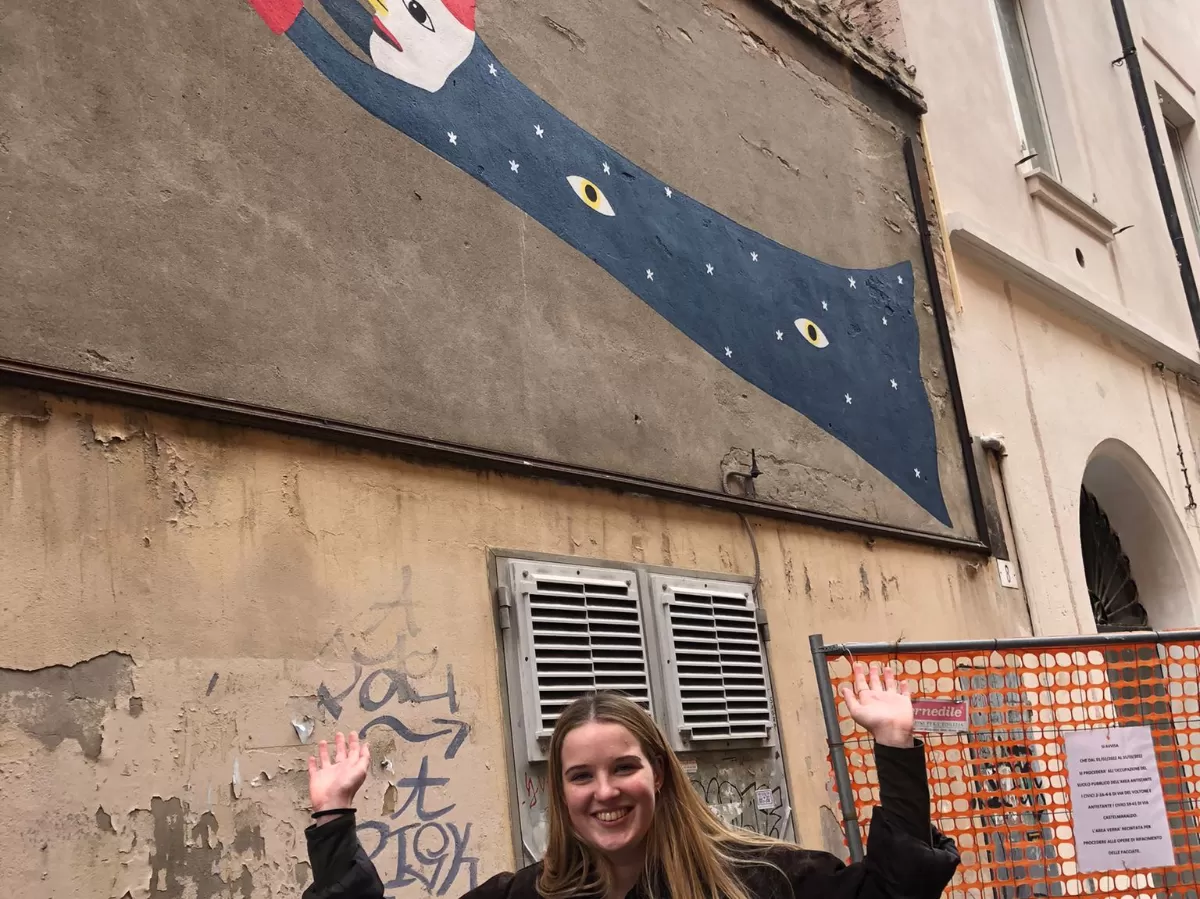 Erasmus student posing in front of a graffiti of a three-eyed duck