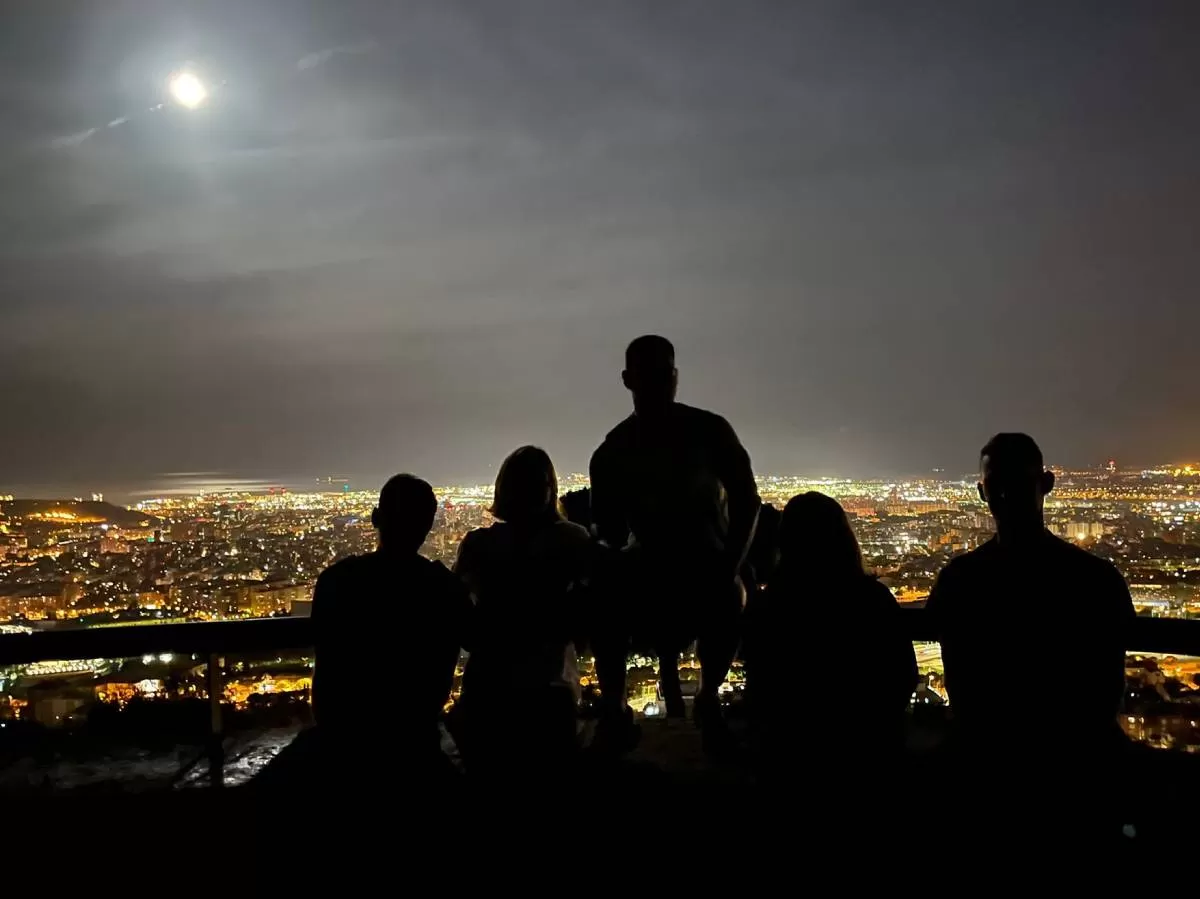 Silhouettes of the five participants with the bright Barcelona skyline behind them. The sky is dark and the photo is only lighting up by the lights of the city.