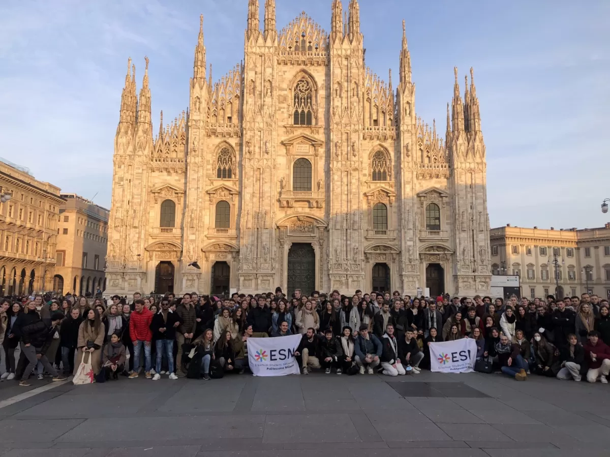 Group of many international students and ESN volunteers posing with the flags in front of Duomo Cathedral