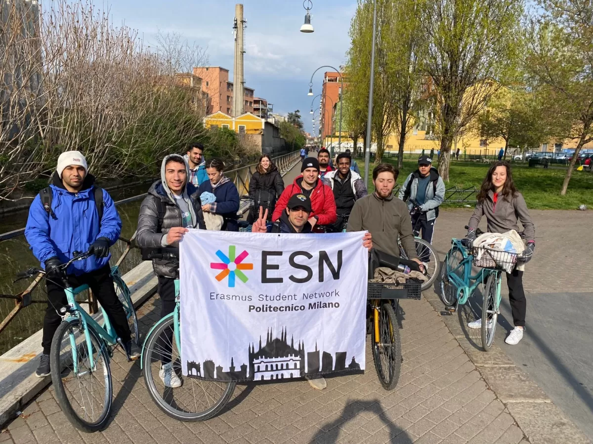 Group of international students and ESN volunteers posing with bikes and flag next to a canal