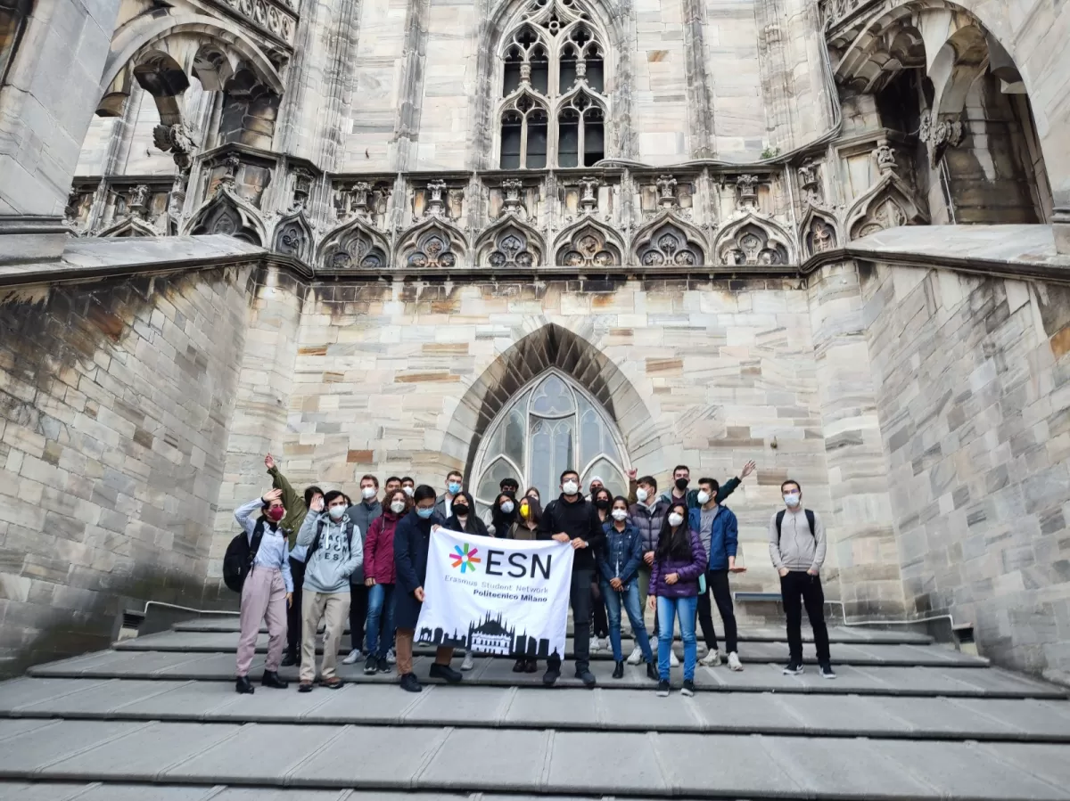 Group of international students and ESN volunteers posing with the flag in front of Duomo cathedral