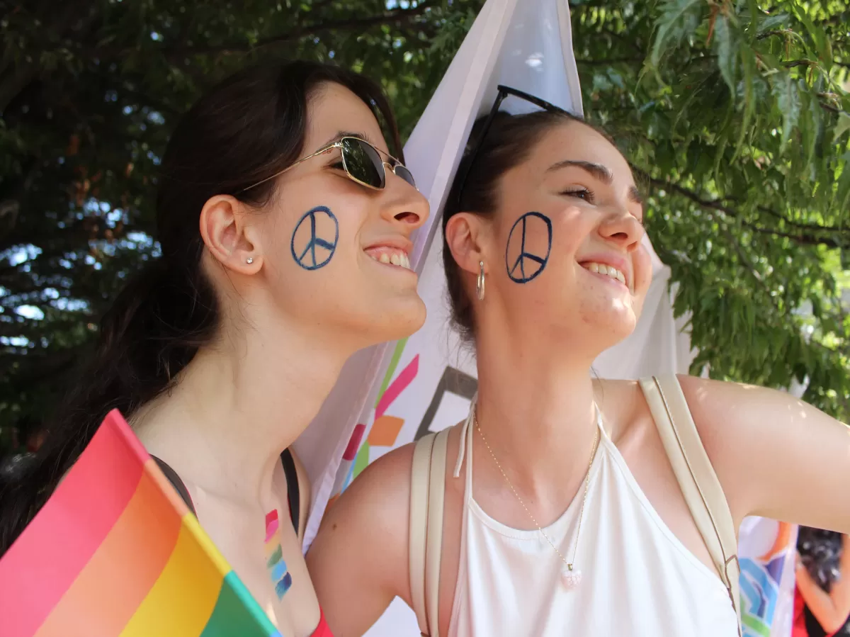 two girls smiling with peace and love symbol painted on their cheeks. LGBTQIA+ and ESN Torino flag