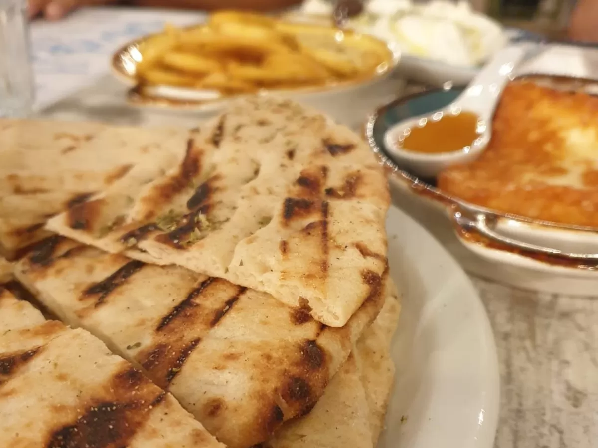 The picture shows typical Greek food: pita bread in the foreground and fried feta with honey in the background, together with some french fries..