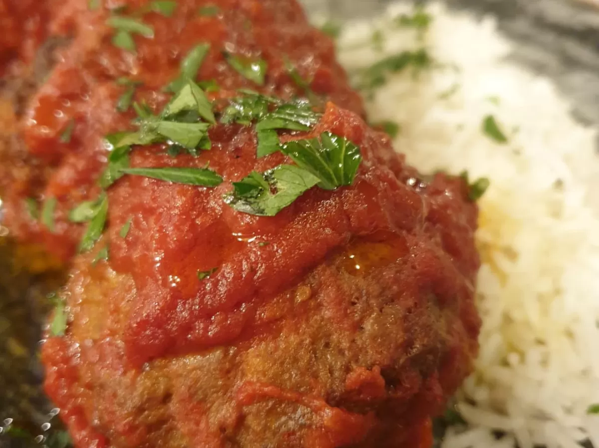 The picture shows Greek meatballs with tomato sauce topped with parsley, and some white rice as a side.