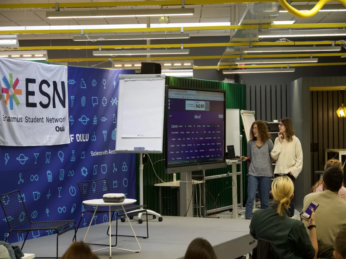 Two student presenters talking about the Kahoot participants' names on the screen in front of an audience who are about the participate in a quiz about Italian culture.