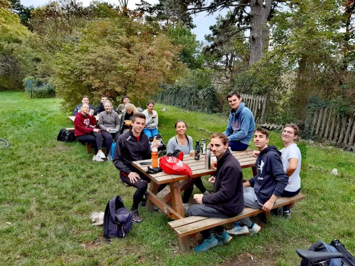 a group of people is sitting on wooden benches with tables on a grass after the bike tour.