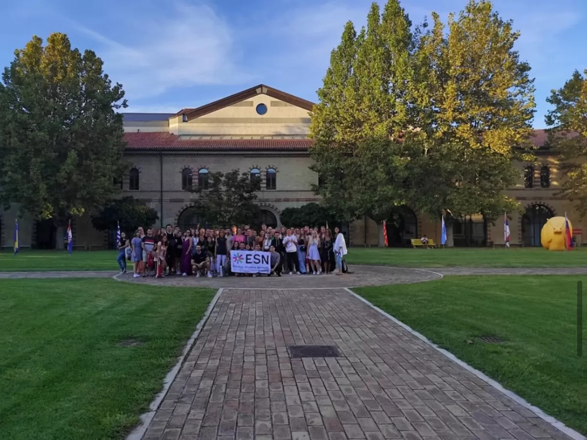 group picture in the middle of the university courtyard. in the middle there is the esnAncona flag.