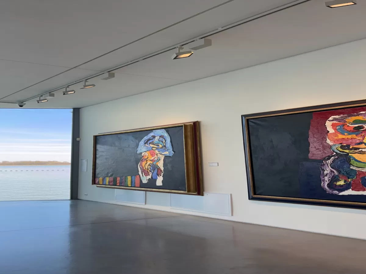 Wall in the gallery with two abstract colourful paintings and view of the river behind