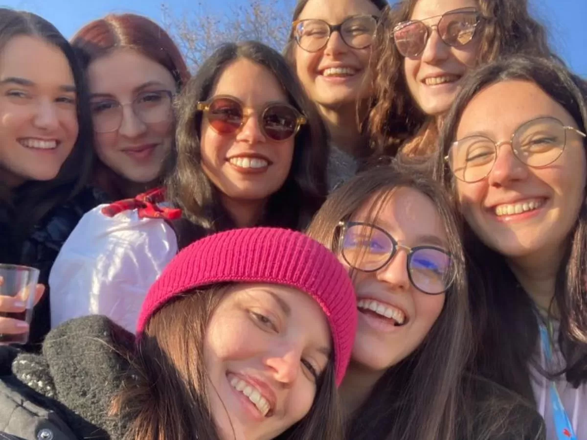 A group of 8 girls is smiling at the camera. In the background there is a bright blue sky.
