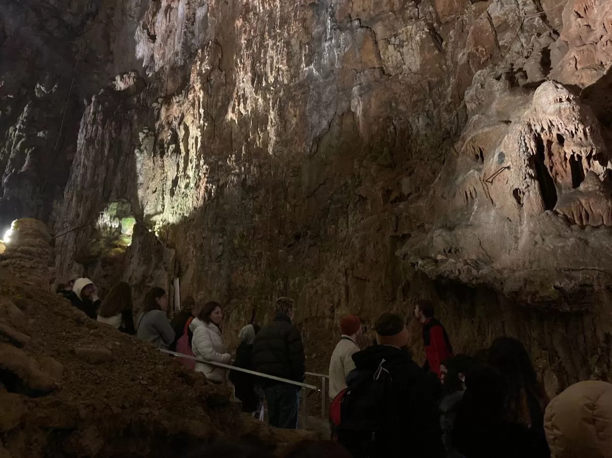 A view of a stone wall of the cave. At the bottom, the participants are standing on the stairs and walking on the side of the wall.
