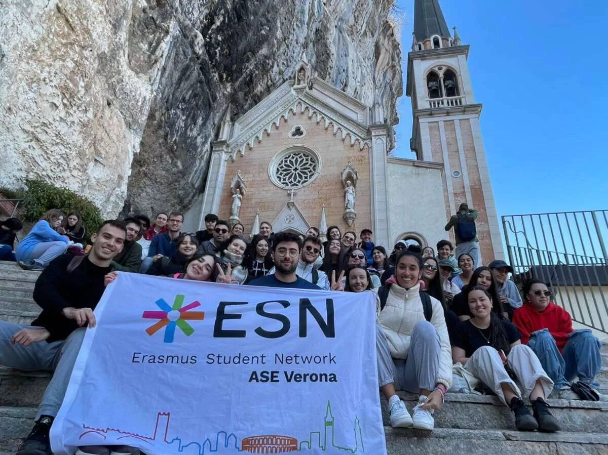 Group of international students sitting in front of the Madonna della Corona Santuary with ESN Verona flag