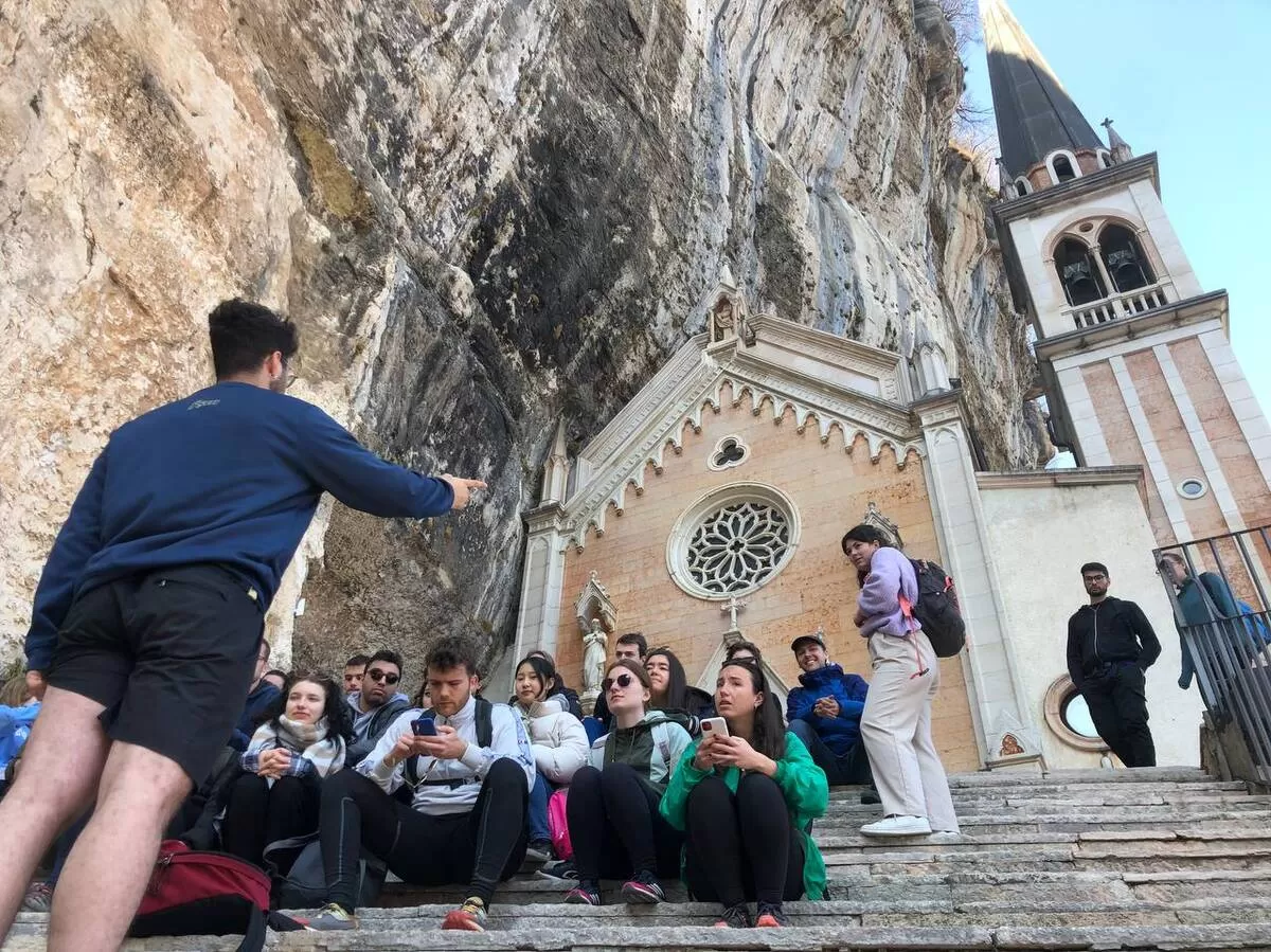Group of international students sitting at the end of the hiking trip in front of the Madonna della Corona Sanctuary