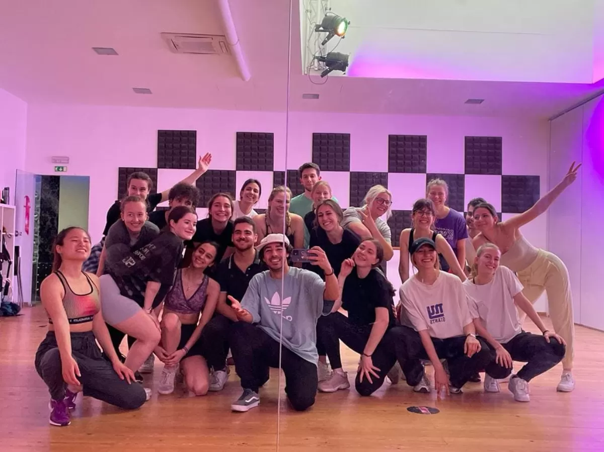 Participants in a dance studio, wearing sports clothes, posing and smiling, with purple lighting