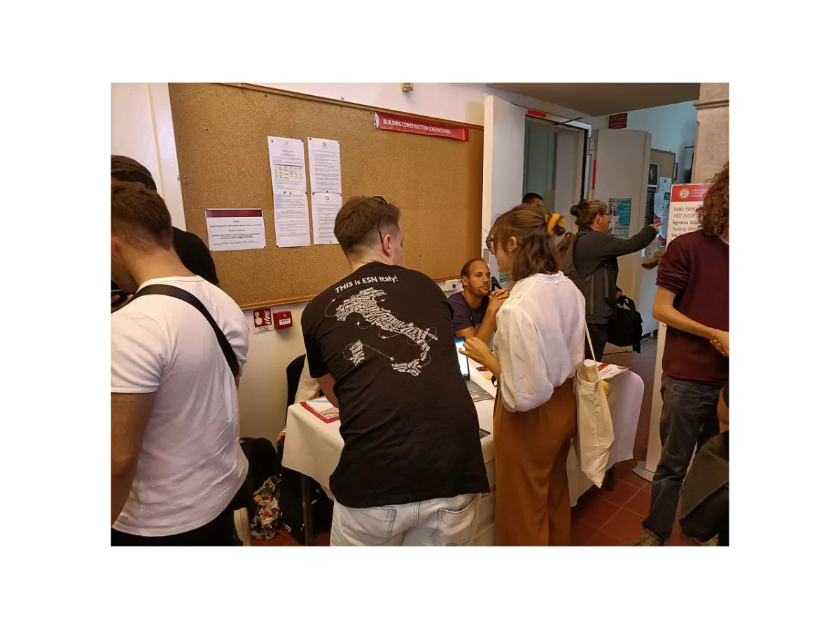 An international students is asking information at the ESN Ravenna's stand. A staff member is helping her. Around them, many people waiting for info