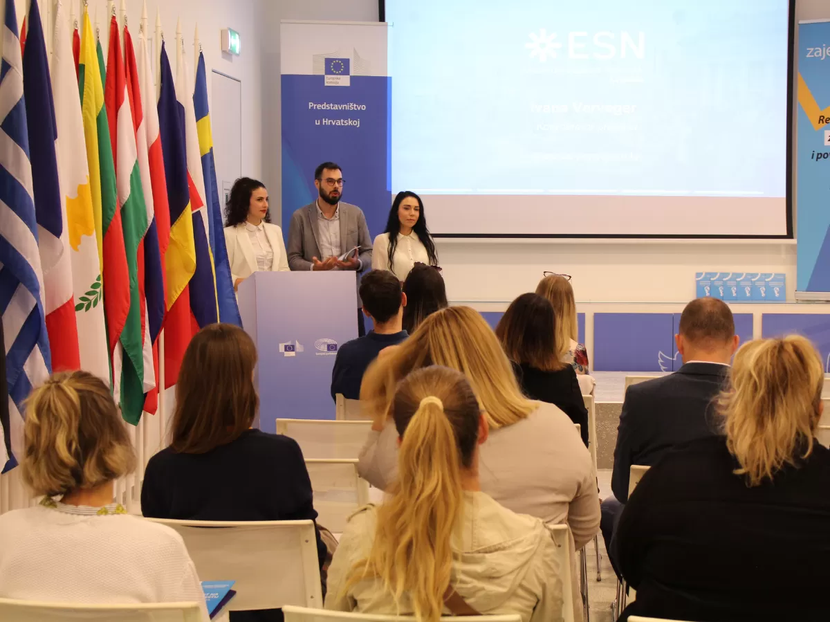 Three volunteers presenting the mobility handbook next to flags of EU countries.