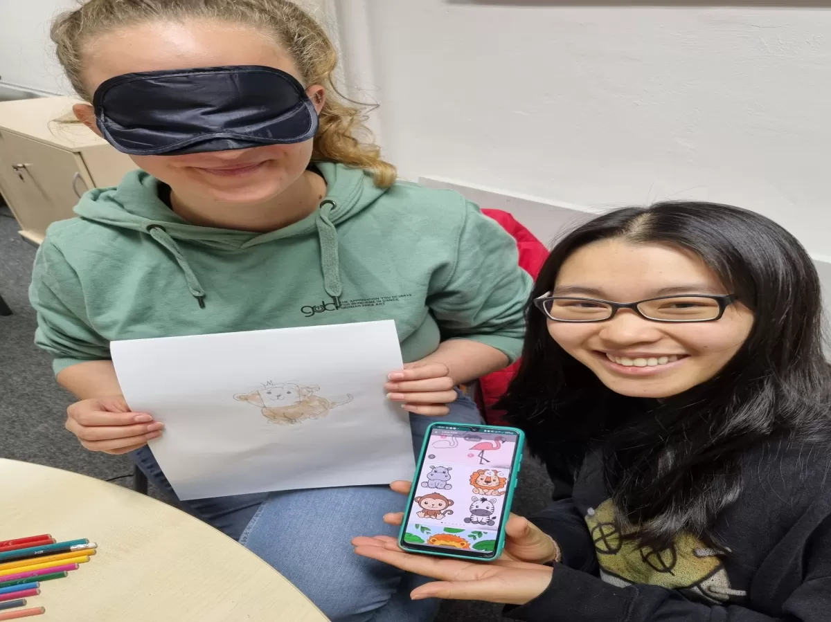 A participant is showing the picture which has been described (monkey) and the blindfolded person shows what she has drawn