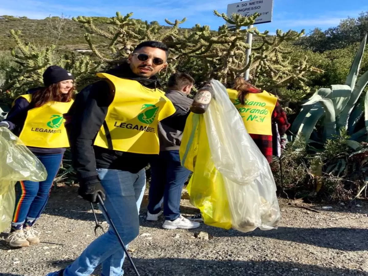 An erasmus student with a trash bag smiles to the camera. In the background there are other students picking up the trash