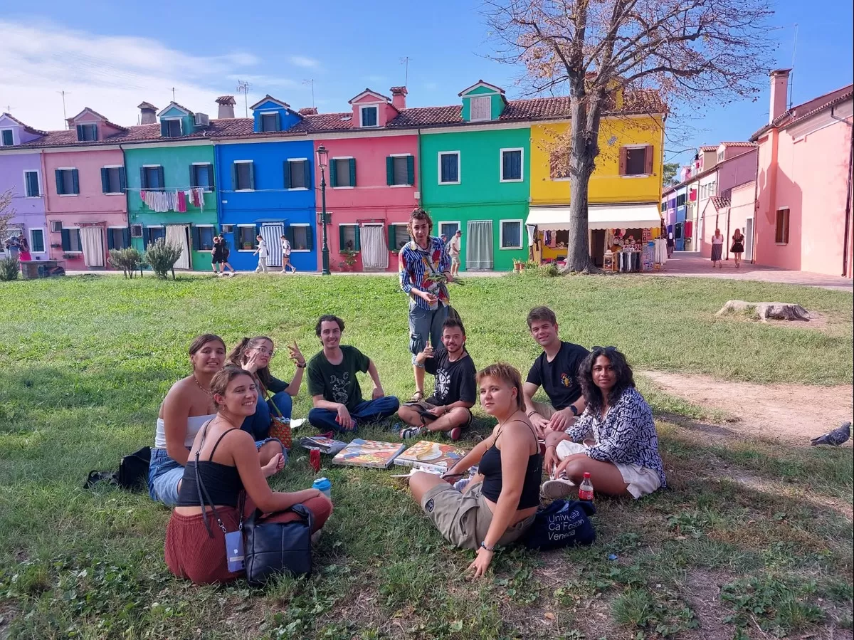 Group of international students sitting on the grass in Burano looking at some of the colorful houses