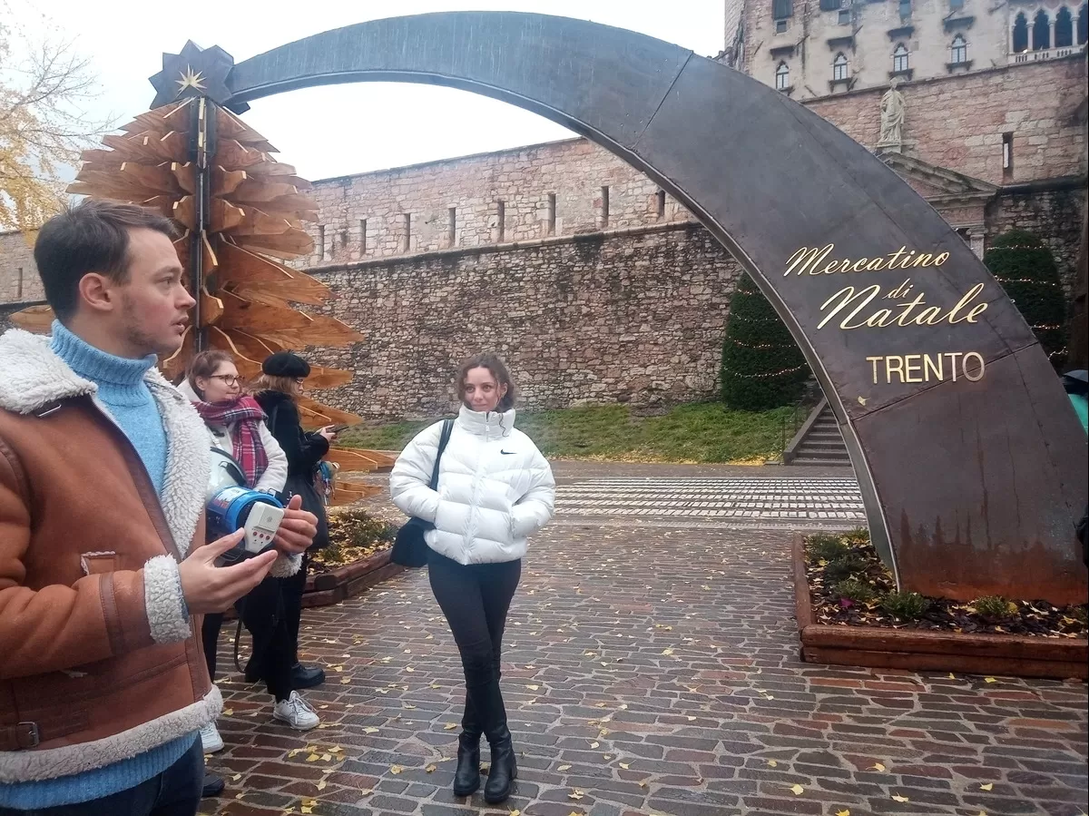 A couple of students standing in front of the Christmas market's sign while listening to the guide