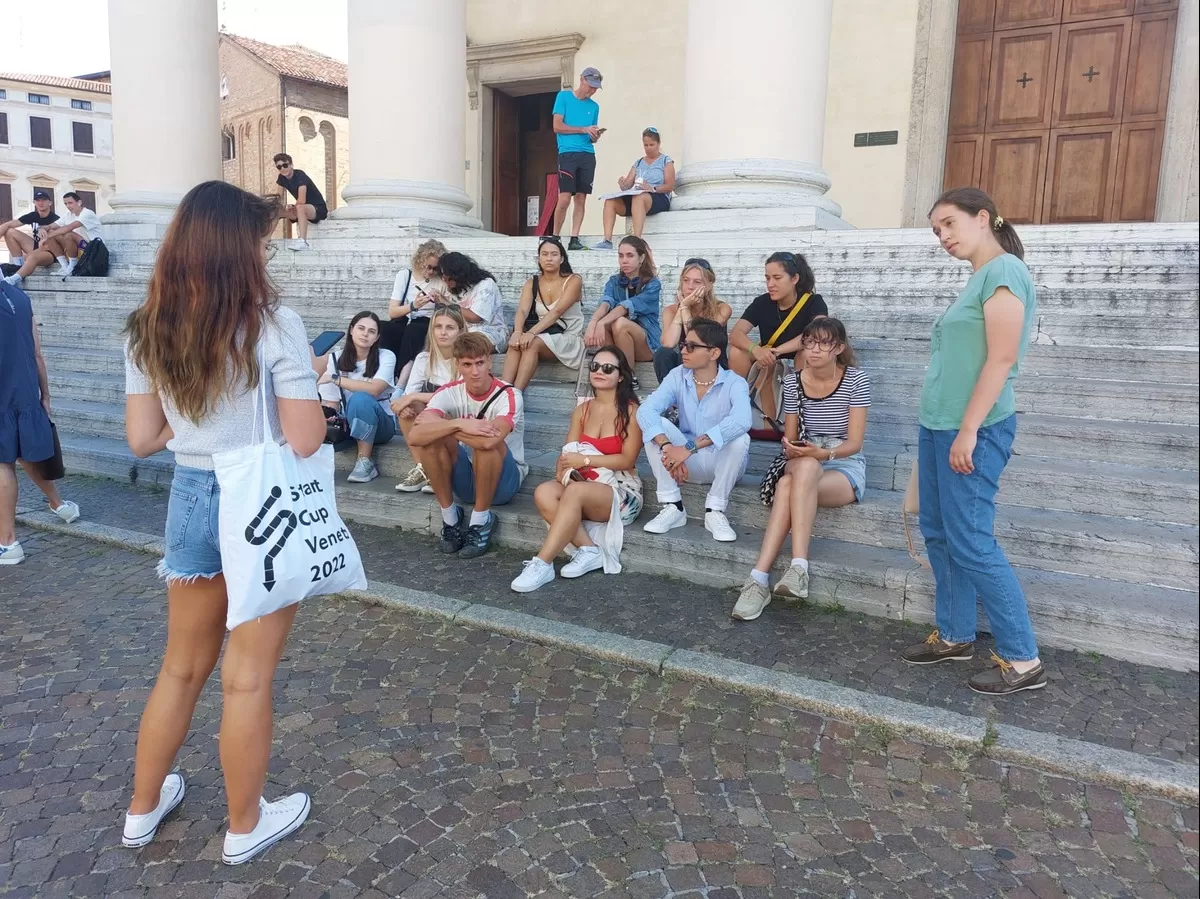 One of the volunteers giving information to the international students who are listening while sitting on the stairs of a curch