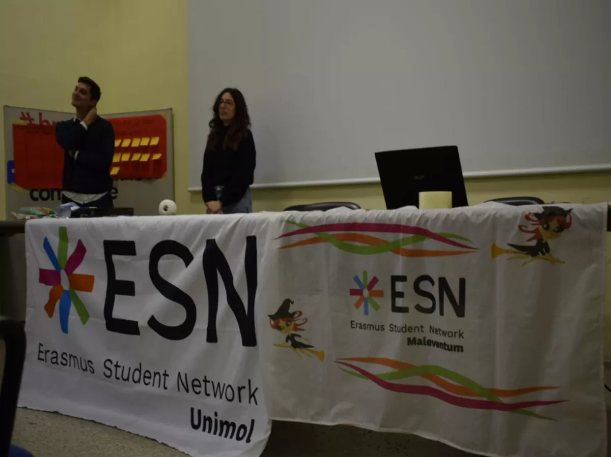 two volunteers giving a speech and in front of them there are the flags of the two ESN sections participating in the event