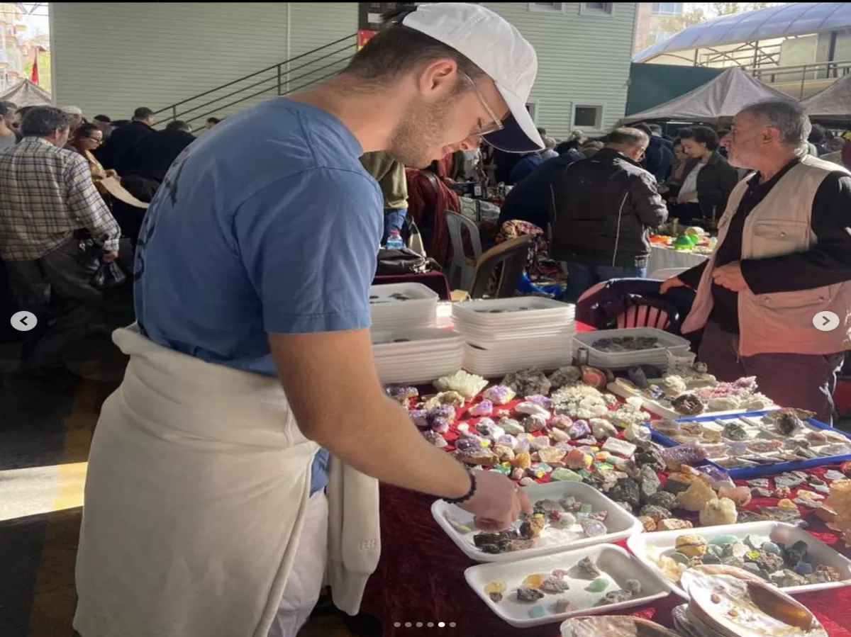 Photo of an Erasmus student looking at small and colorful Cristals on the table. A vendor is seen in the background.