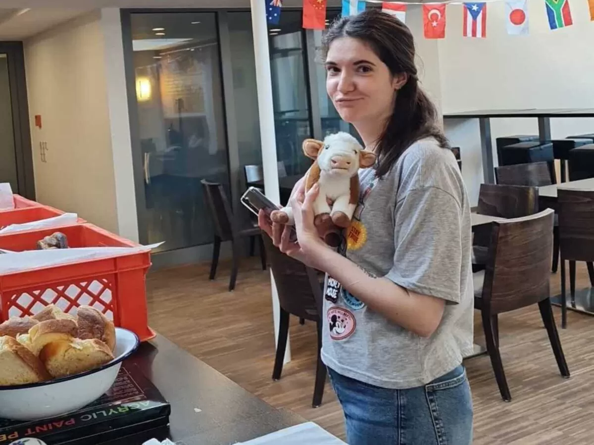A person with a cow plushie standing next to a table with bread.
