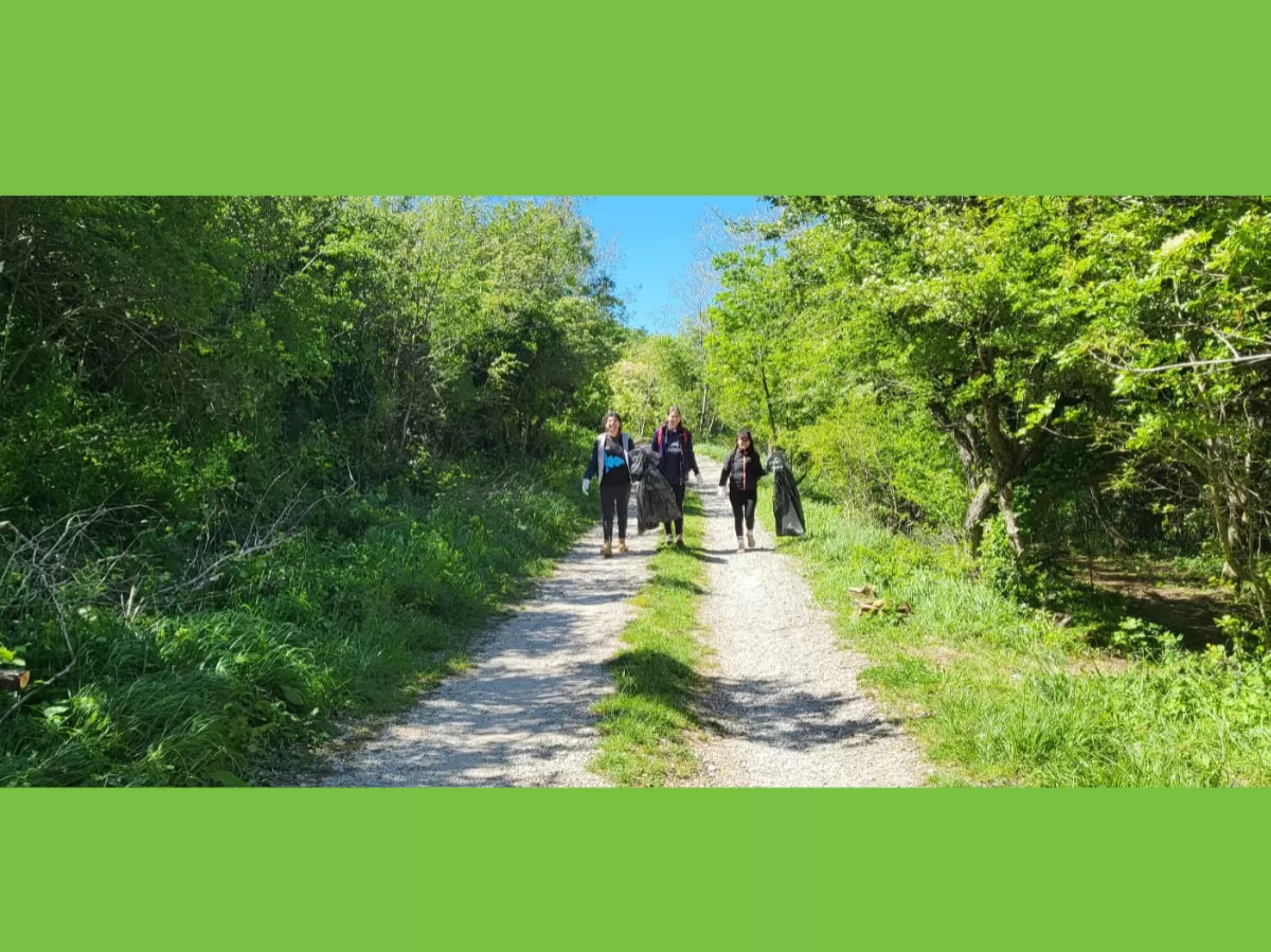 Three girls at some distance are walking towards the camera along one of the paths where garbage was collected. They smile and hold the plastic bags full of waste