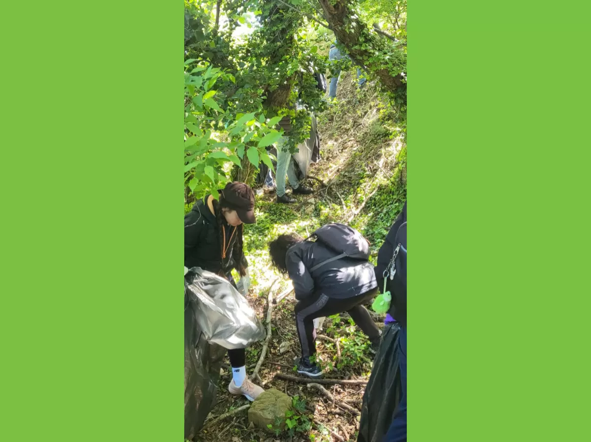 Two more participants collecting waste from the ground. The one on the left is holding the bag and the one on the right is leaning forward towards her