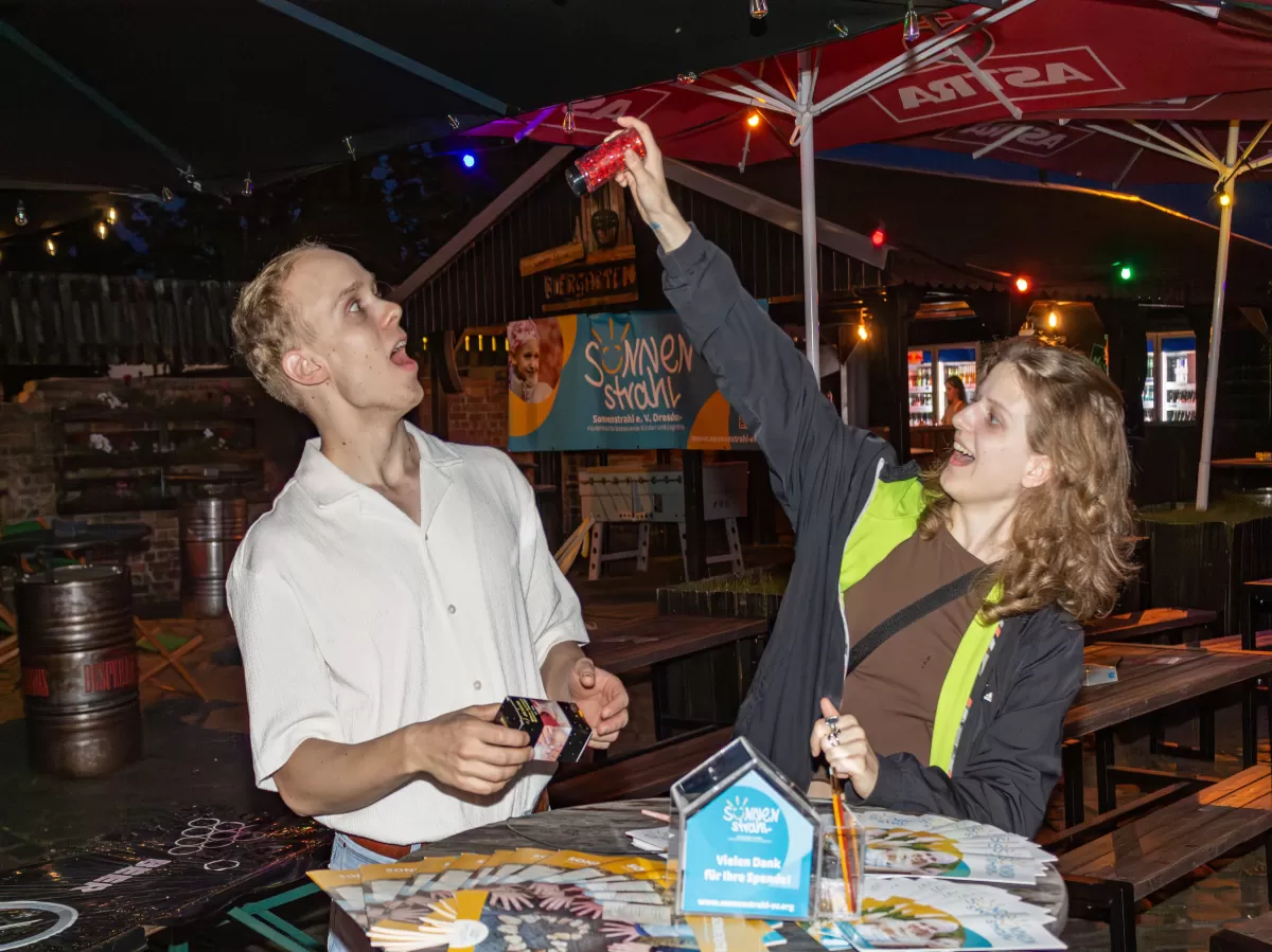 2 persons at round table with flyers looking at each other and making fun