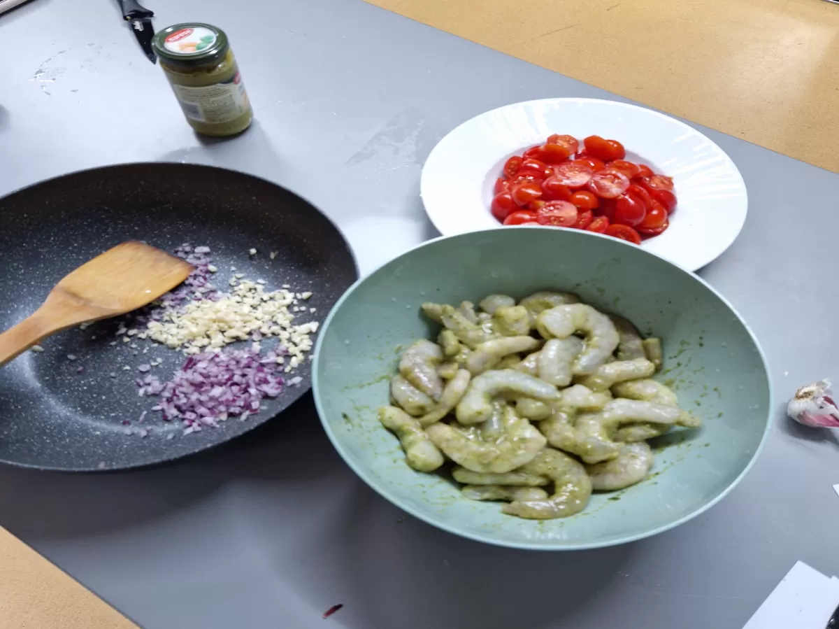 Garlic and onion on a pan, shrimp in a bowl, cherry tomatoes cut in half in a bowl