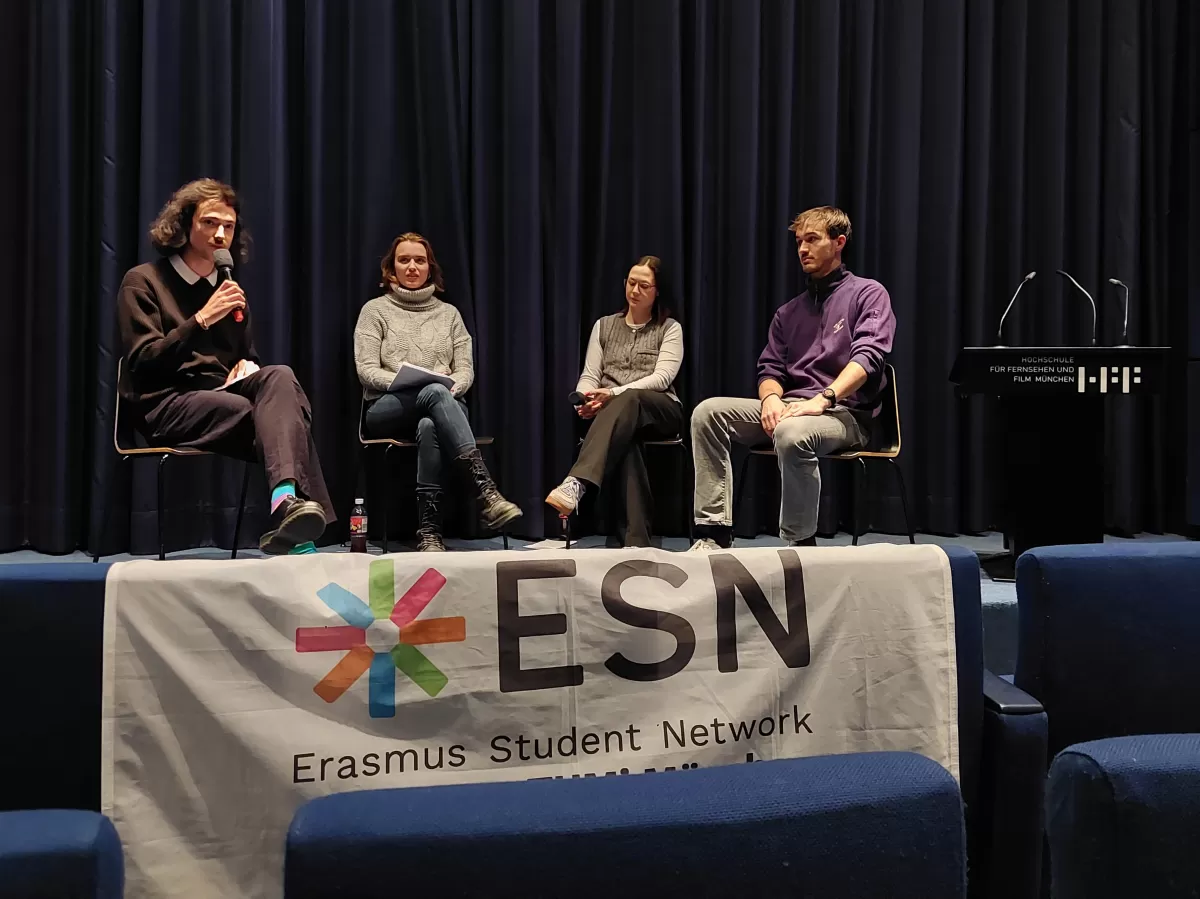 Four people sitting in front of a cinema screen for a panel discussion. First person is speaking in a microphone. ESN section flag is hung in the bottom of the picture.