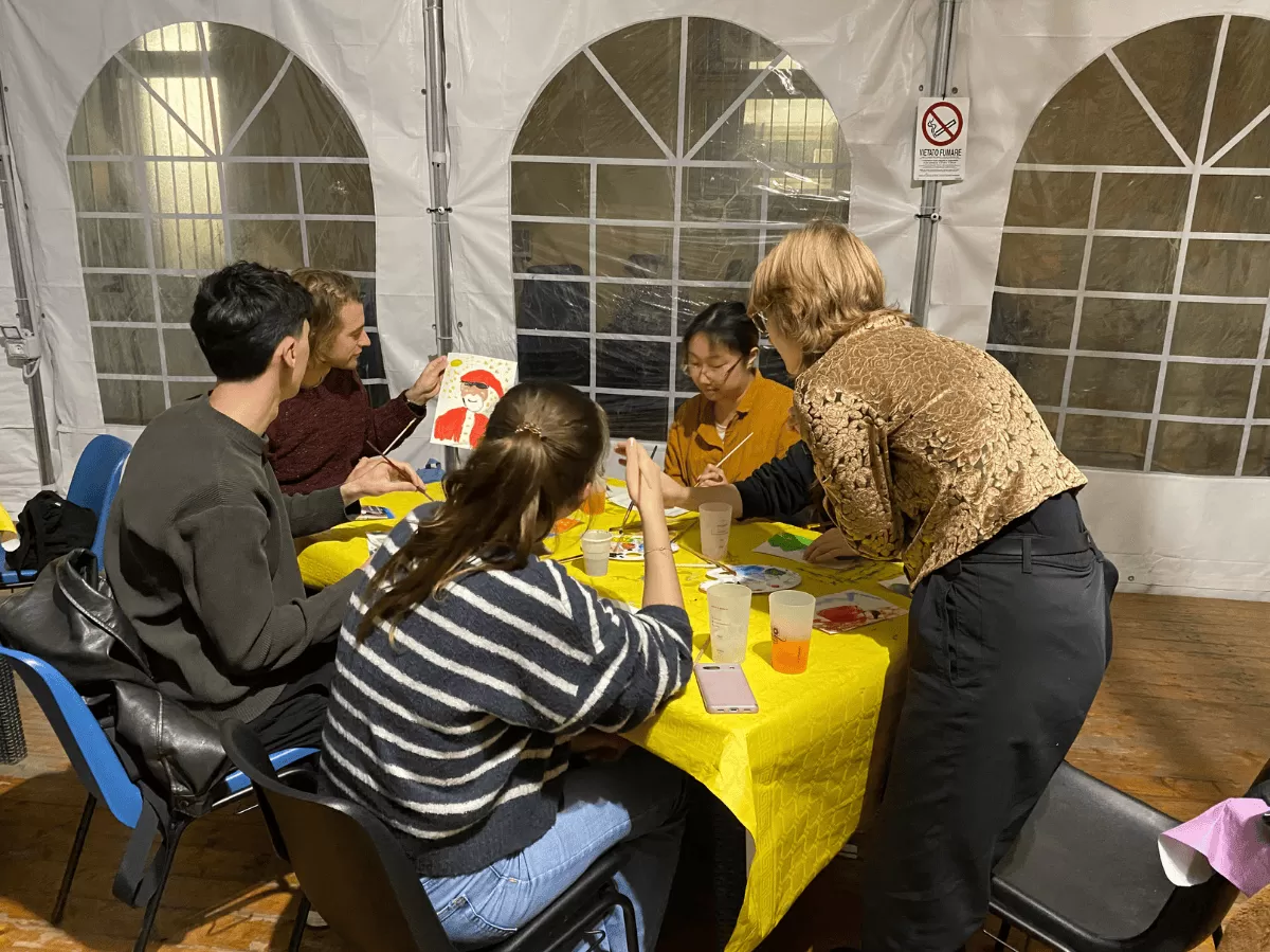 group of students paiting, one student is showing a painting of Santa Claus he made