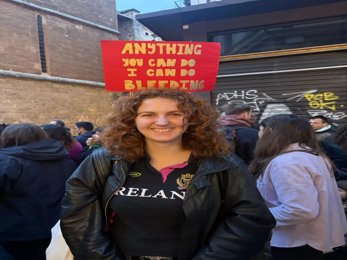 International student holding a banner that says "Anything you can do, I can do bleeding"