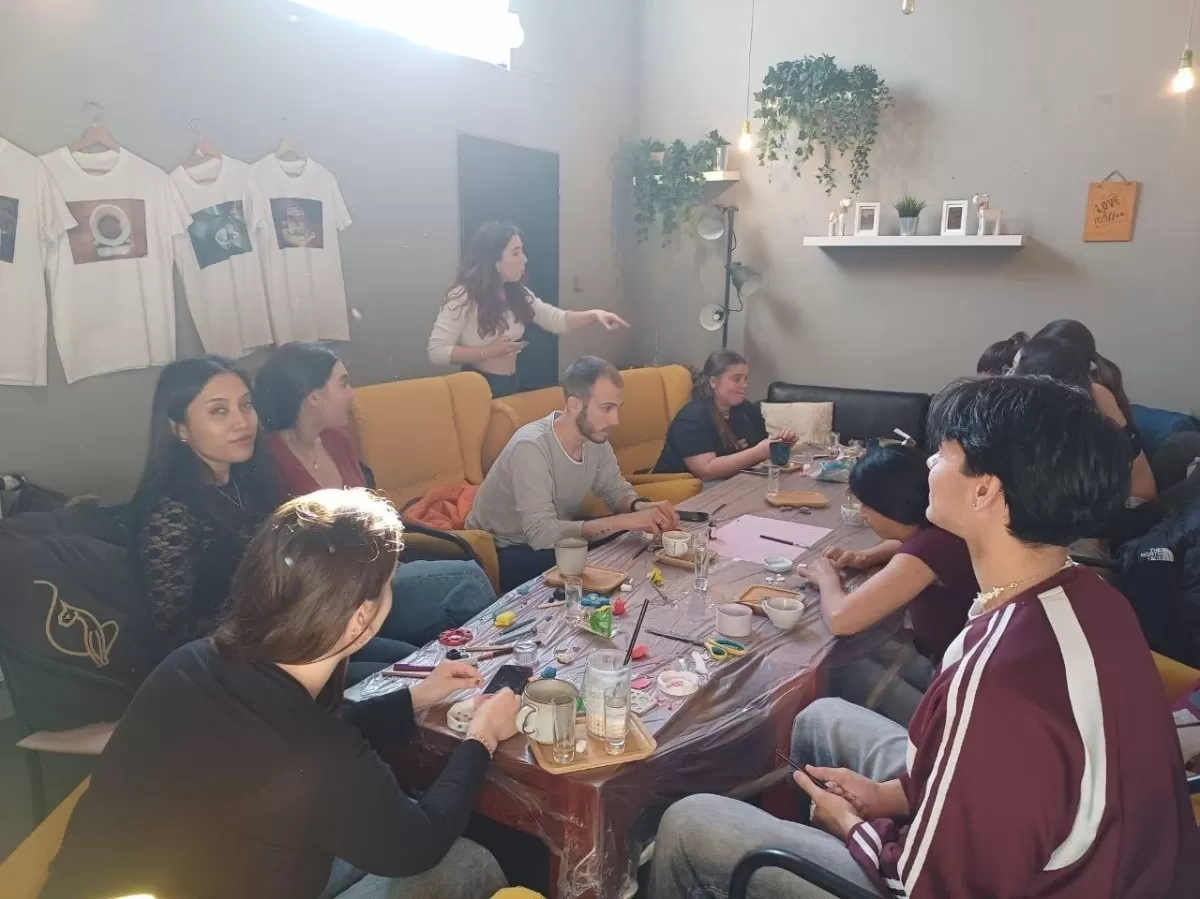 a few people in a cafe sitting in a circle at the table crafting with clay