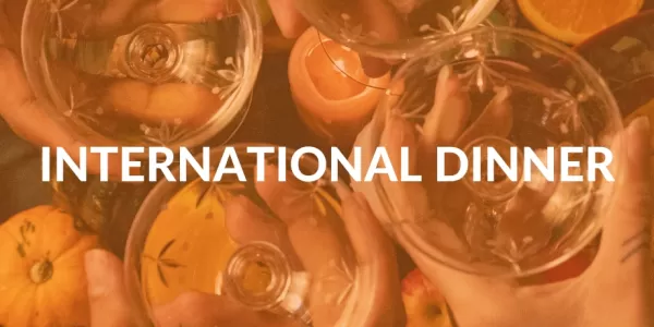 There's a table filled with different types of food from different nationalities, faded behind ESN's orange colour. International Dinner is written in the middle of the picture.