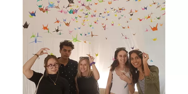 Group photo taken inside the origami lab surrounded by many hanging cranes